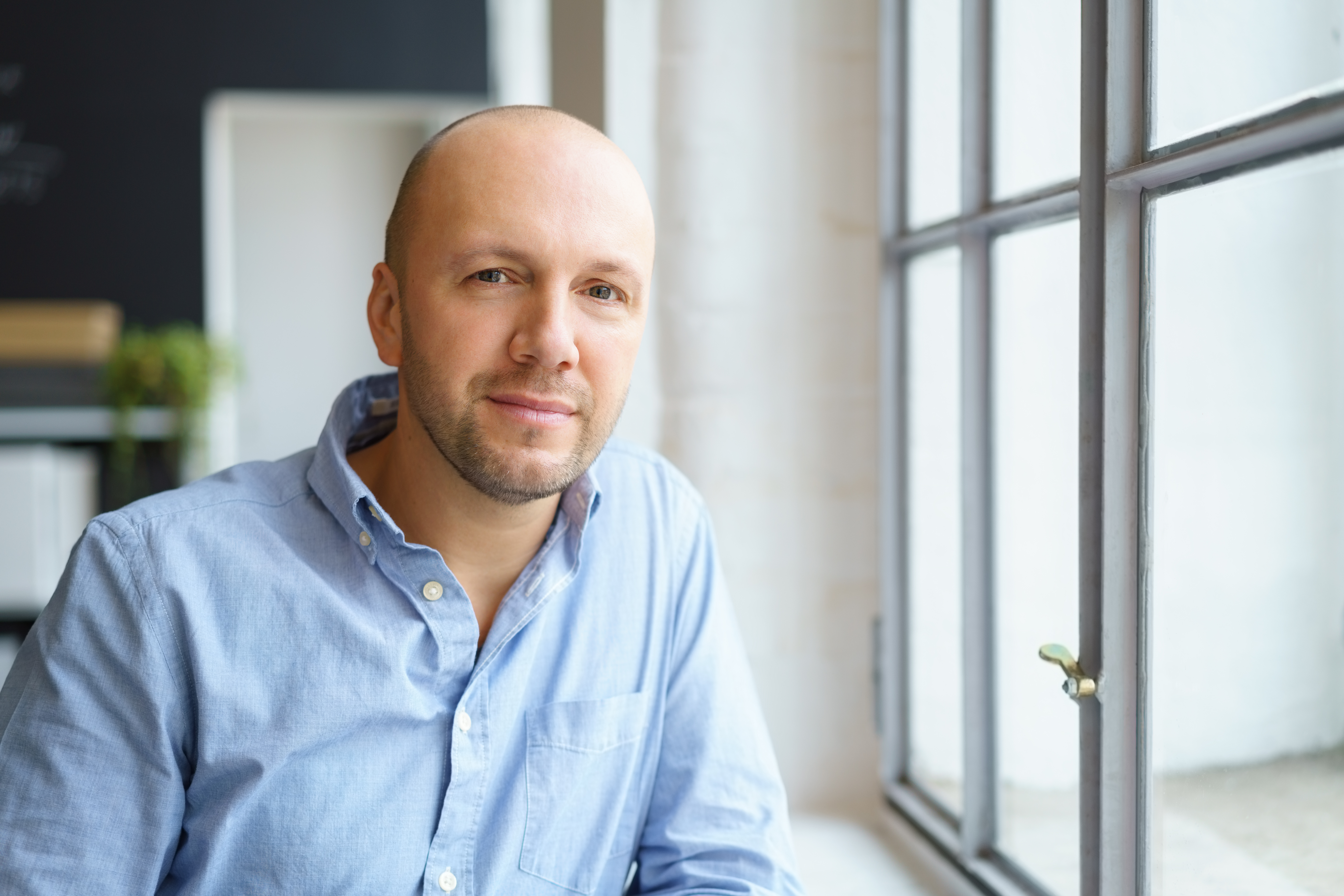Fotografi från ett kontor. I bilden syns en man i skjorta. Han tittar in i kameran och ler nöjt och tryggt.